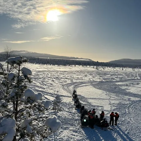 A line of snowmobiles on the trail under a low sun