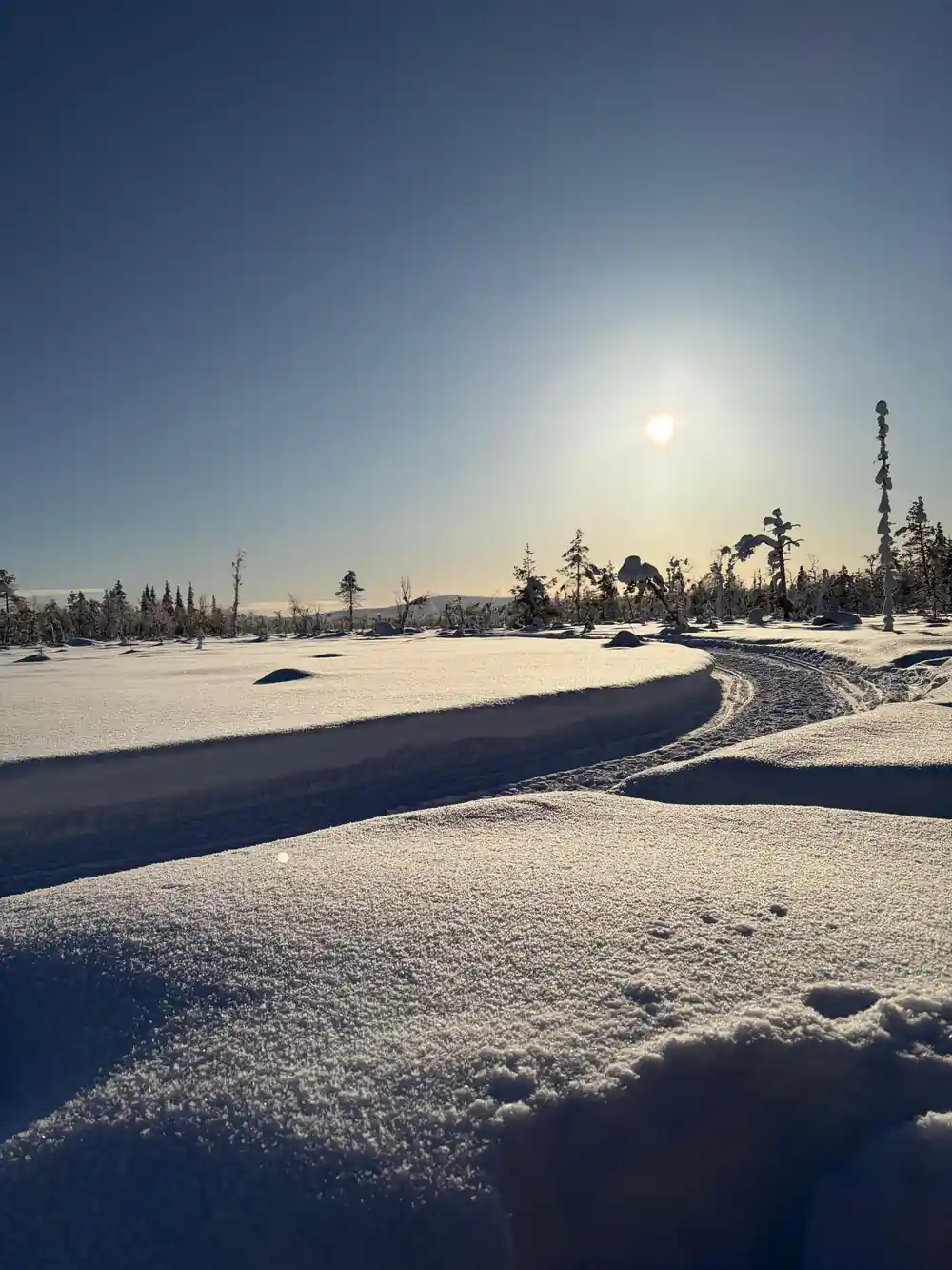 Low winter sun over an empty snow plain with a trail curving away