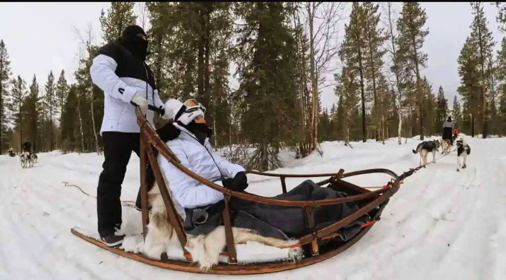 Passenger wrapped in a rug sitting in a wooden sled basket in forest