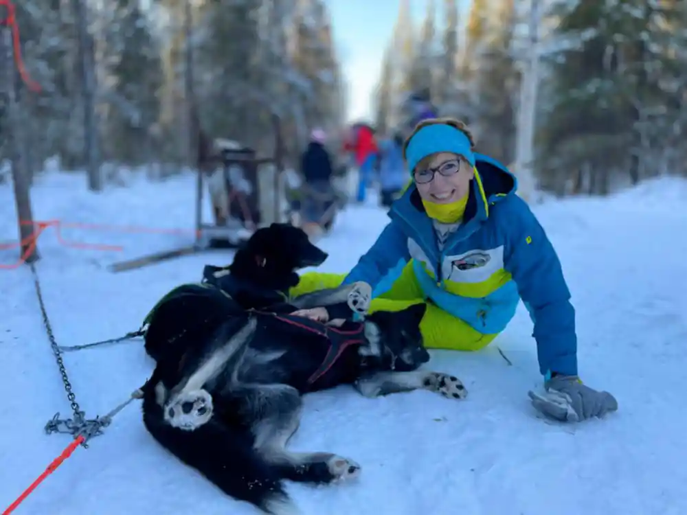 Visitor in blue kneeling beside dogs lying in the snow