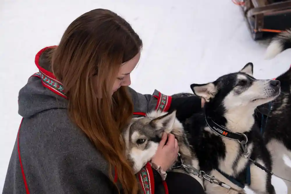Visitor with long red hair leaning down to a husky among the team